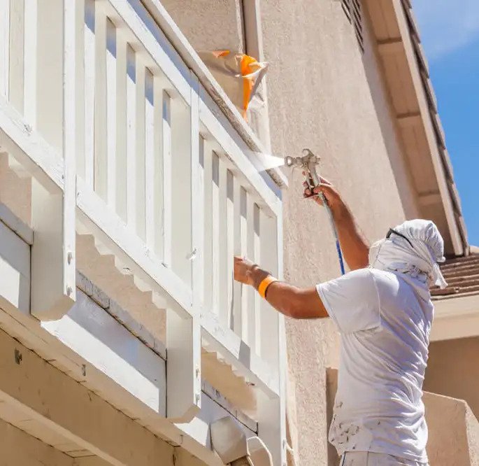 Worker spray painting home exterior